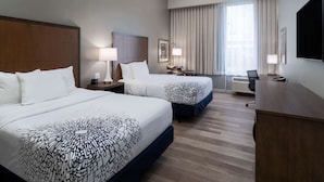 Una habitación de hotel con dos camas, un escritorio, una silla, un televisor y una ventana con cortinas.