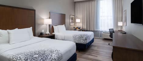 Una habitación de hotel con dos camas, un escritorio, una silla, un televisor y una ventana con cortinas.
