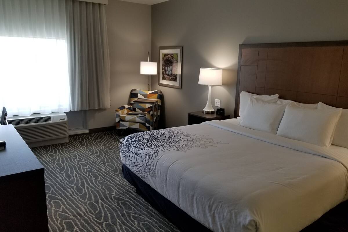 A hotel room with a large bed, two bedside lamps, a patterned rug, a desk, and a chair.