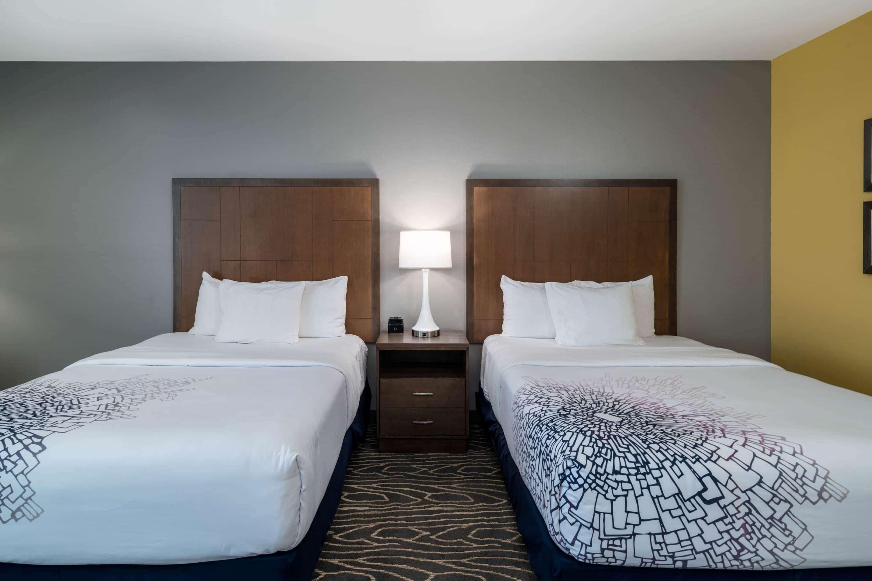 A hotel room with two beds, a nightstand with a lamp, and a patterned carpet.