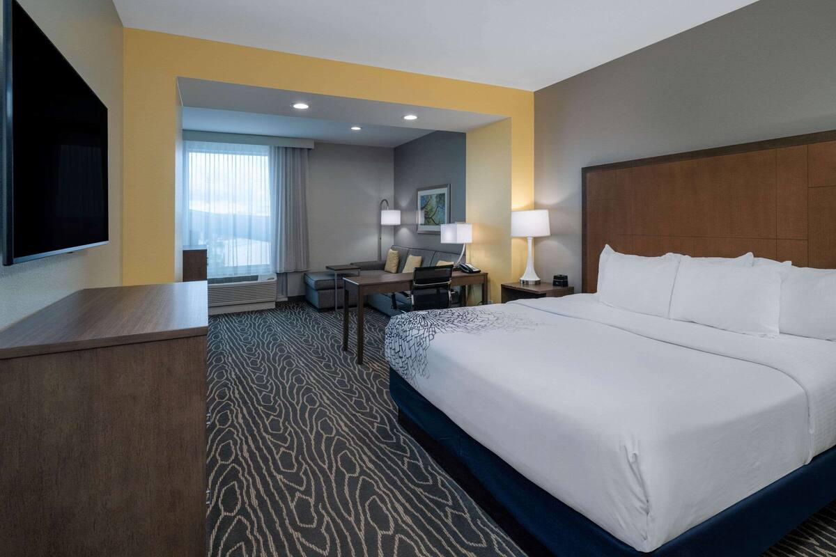 A hotel room with a large bed, a desk, a chair, a TV, and a window with curtains.