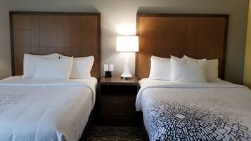 Une chambre d’hôtel avec deux lits, une table de chevet avec une lampe et un tapis à motifs.