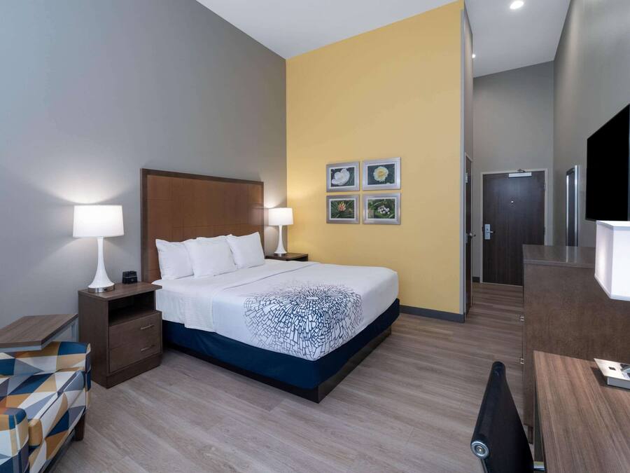 A hotel room with a bed, two bedside tables with lamps, a chair, a desk, and a TV.