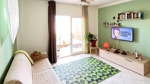 A living room with a sofa, a television, a ceiling fan, a patterned rug, and a bookshelf. - PORT DO SOL - free wifi NO LIMITS (Contea di Boa Vista)