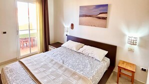 A bedroom with a bed, a ceiling fan, a window with curtains, a wall-mounted light, and a small wooden stool. - PORT DO SOL - free wifi NO LIMITS (Contea di Boa Vista)