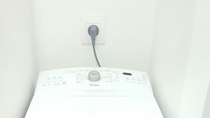 Eine weiße Whirlpool Waschmaschine in einem Raum mit weißer Wand und einem sichtbaren Stromanschluss darüber.