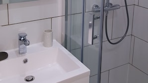 Ein modernes Badezimmer mit Duschkabine aus Glas, einem weißen Waschbecken mit Spiegel darüber und einem Handtuchhalter.