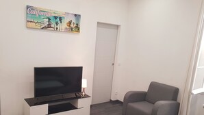 Ein Wohnzimmer mit Flachbildfernseher auf einer weißen Unterhaltungseinheit, einem grauen Sessel und einem weißen Couchtisch.