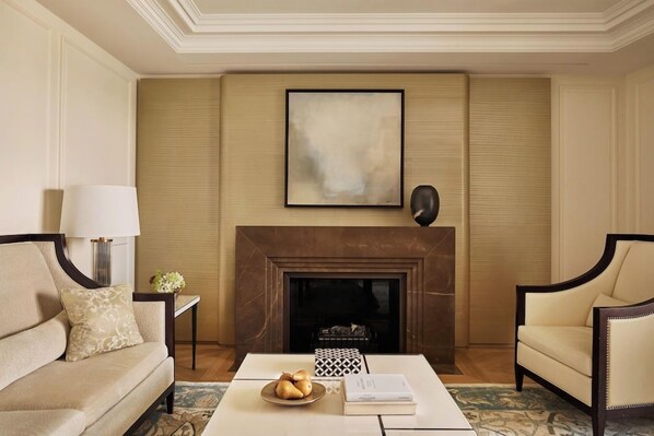 A living room with a fireplace, a sofa, a coffee table with books and fruit, and a lamp. - The Woodward An Oetker Collection Hotel (Geneva)
