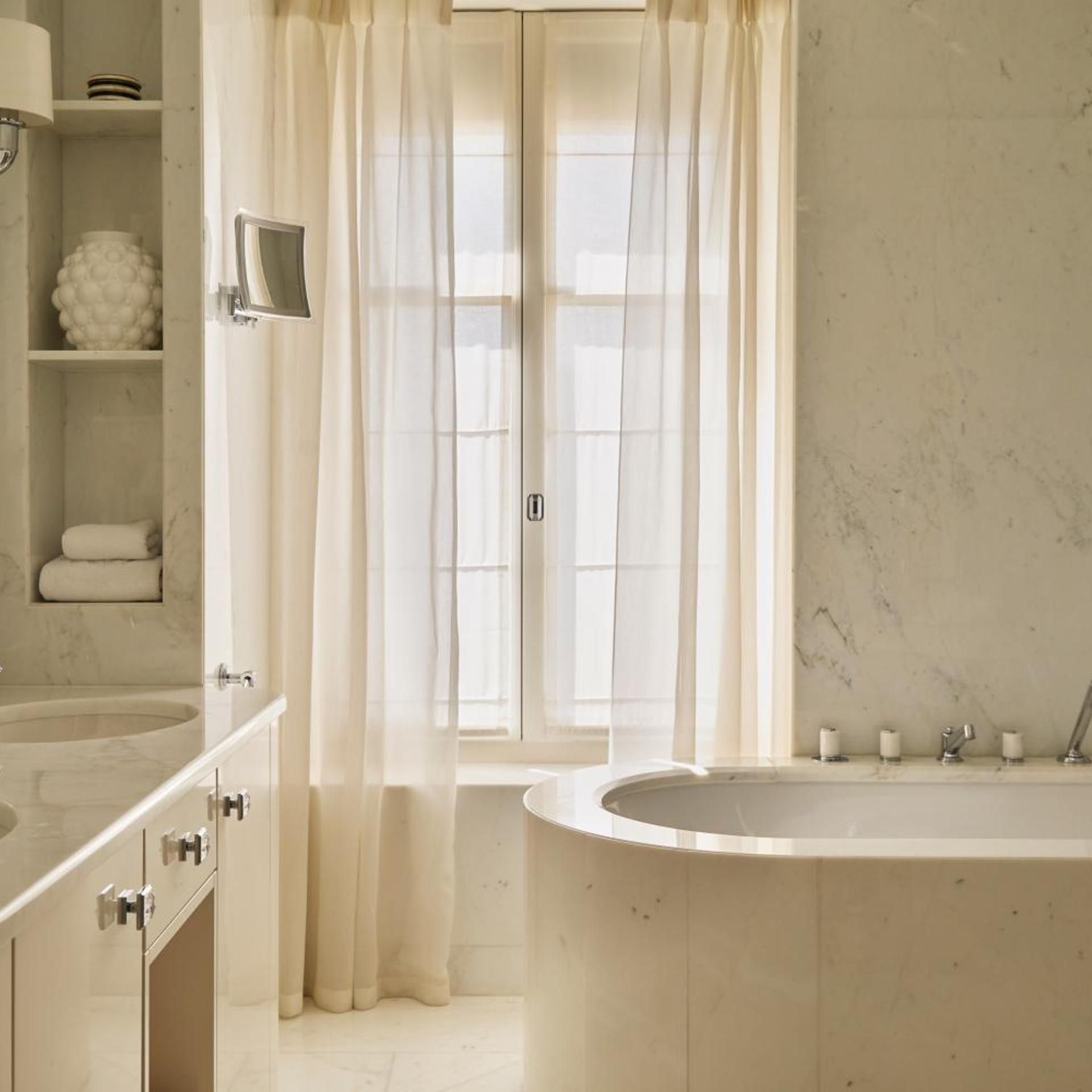 A bathroom with a freestanding bathtub, a vanity with a mirror, and a window with sheer curtains.