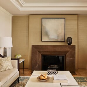 A living room with a sofa, a coffee table with a bowl of fruit, a fireplace, and a framed abstract painting. - The Woodward An Oetker Collection Hotel (Geneva)
