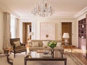 A spacious living room with a large chandelier, a sofa set, a coffee table, and a bookshelf. - The Woodward An Oetker Collection Hotel (Geneva)