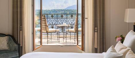 A hotel room with a large bed, a view of a balcony with outdoor furniture, and curtains on the windows.
