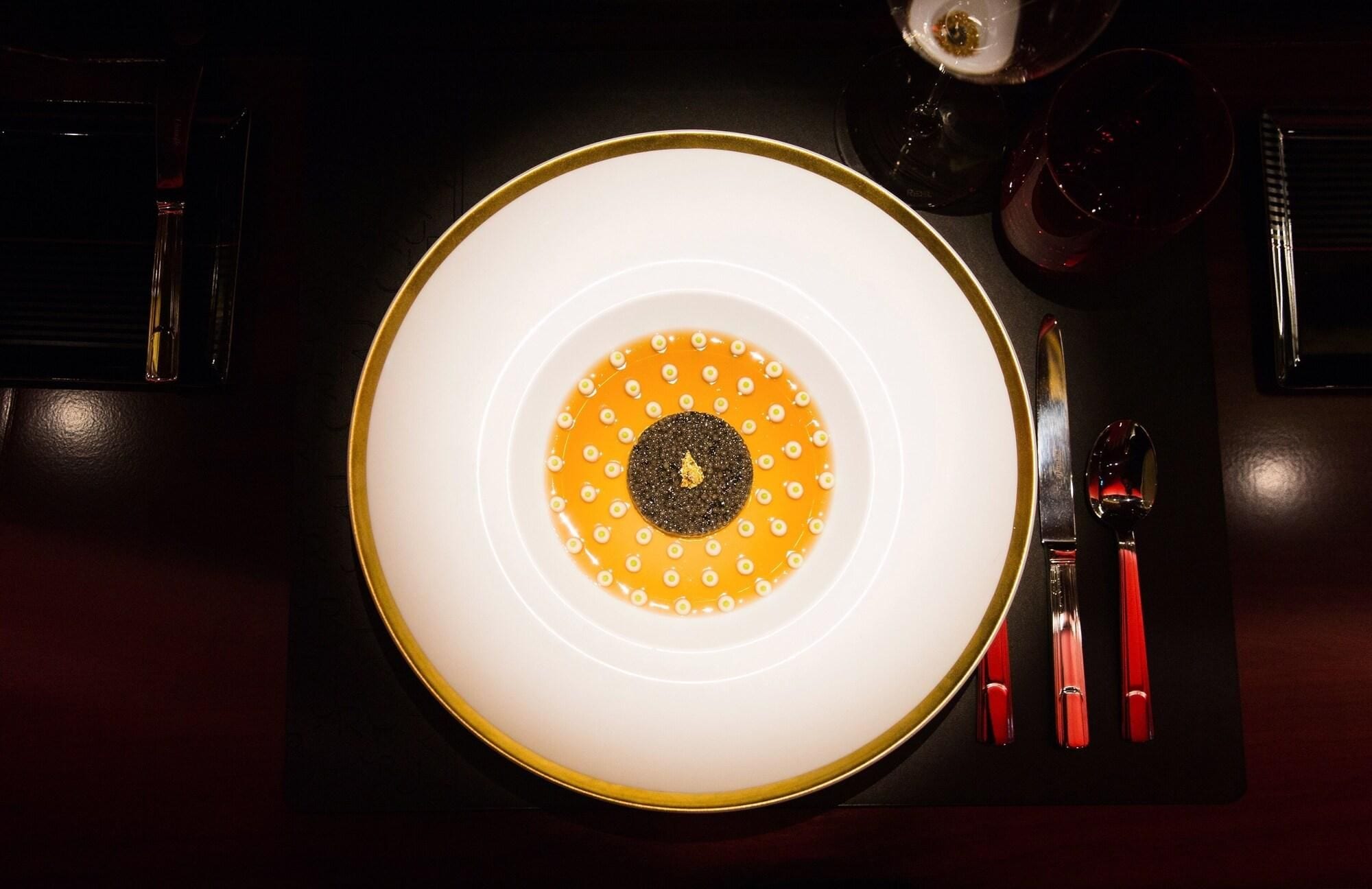 Un plato blanco con borde dorado, un círculo negro central y puntos amarillos dispuestos en un diseño circular.