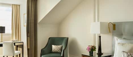 A hotel room with a bed, a desk, a chair, and a nightstand with a lamp.