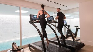 Two people using treadmills in a modern gym with large windows and a view of a pool. - The Woodward An Oetker Collection Hotel (Geneva)