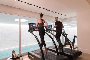 Two people using treadmills in a modern gym with large windows and a view of a pool. - The Woodward An Oetker Collection Hotel (Geneva)
