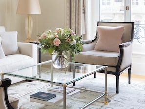 A living room with a glass coffee table, a beige sofa, a dark armchair, and a vase with flowers. - The Woodward An Oetker Collection Hotel (Geneva)