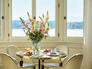 A dining table with a vase of flowers, plates of food, and a view of mountains through large windows. - The Woodward An Oetker Collection Hotel (Geneva)