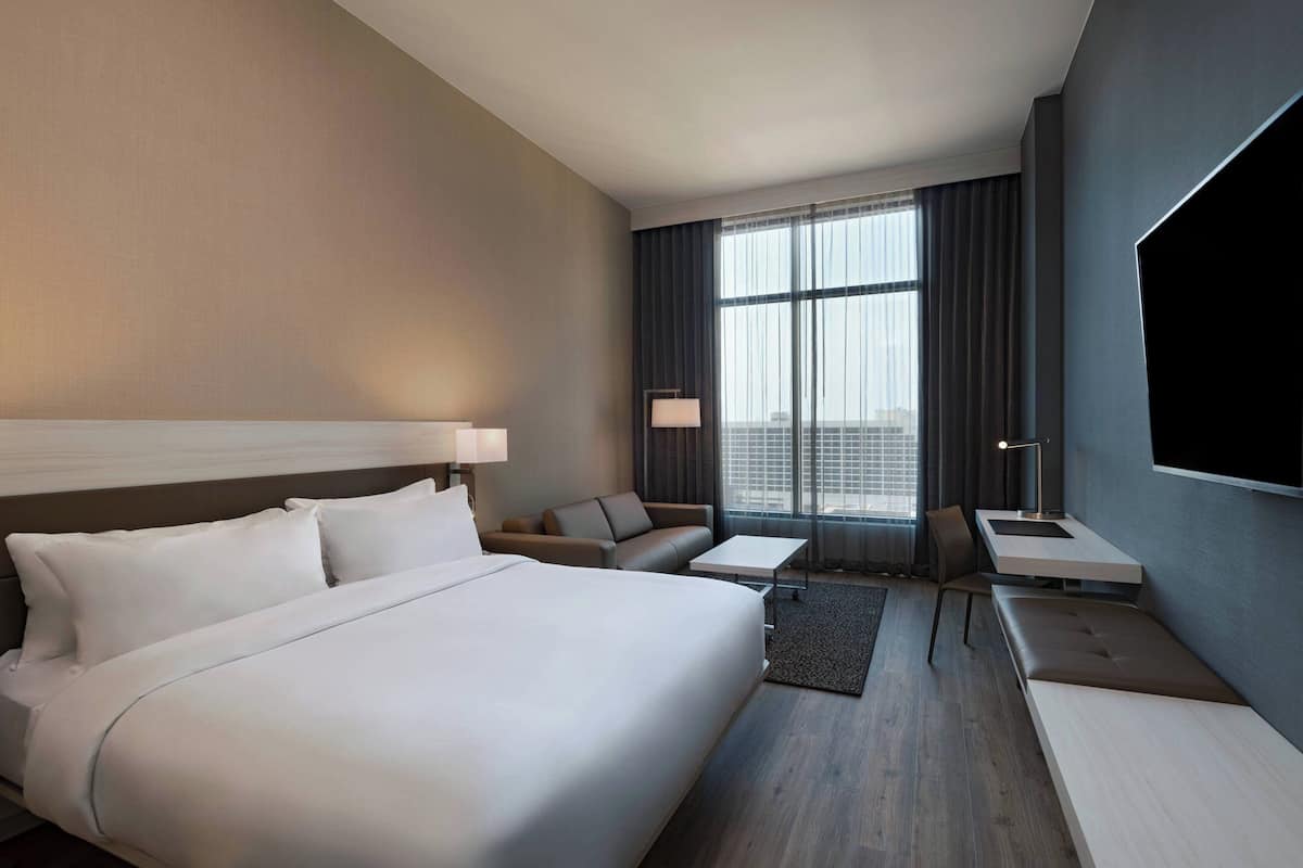 A modern hotel room with a large bed, a desk, a sofa, and a TV.
