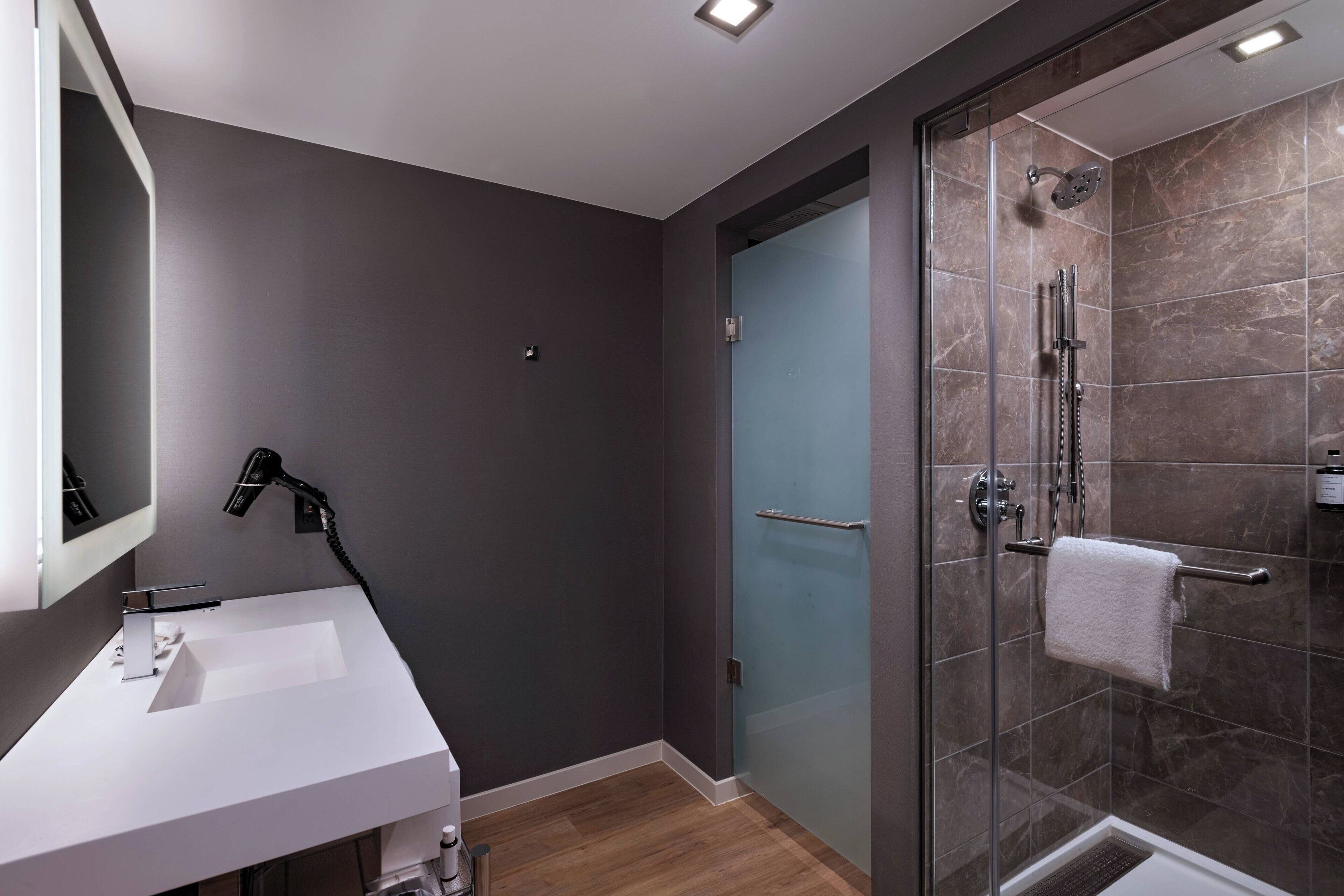A modern bathroom with a white sink, a glass shower enclosure, and a dark wall.