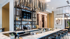 A bar area with a marble countertop, multiple stools, and a variety of bottles and jars on shelves.