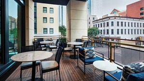 A covered outdoor seating area with tables and chairs, overlooking a cityscape.