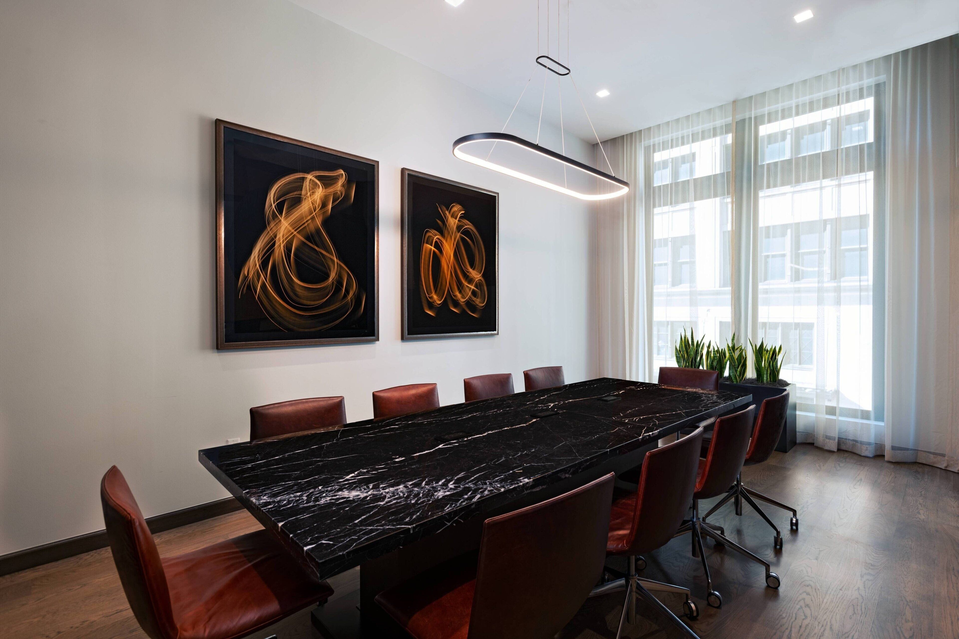 A conference room with a long table, red chairs, and two abstract paintings on the wall.