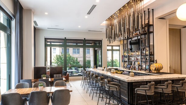 A modern bar area with a long counter, multiple stools, and a large window offering a view of the city.