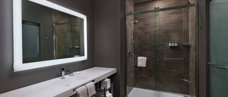 Un baño moderno con un espejo grande, un lavabo blanco y una ducha con mampara de vidrio.