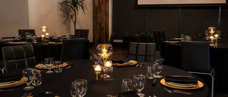 A conference room with round tables set for a meeting. Each table has a projector screen, chairs, and a plant.