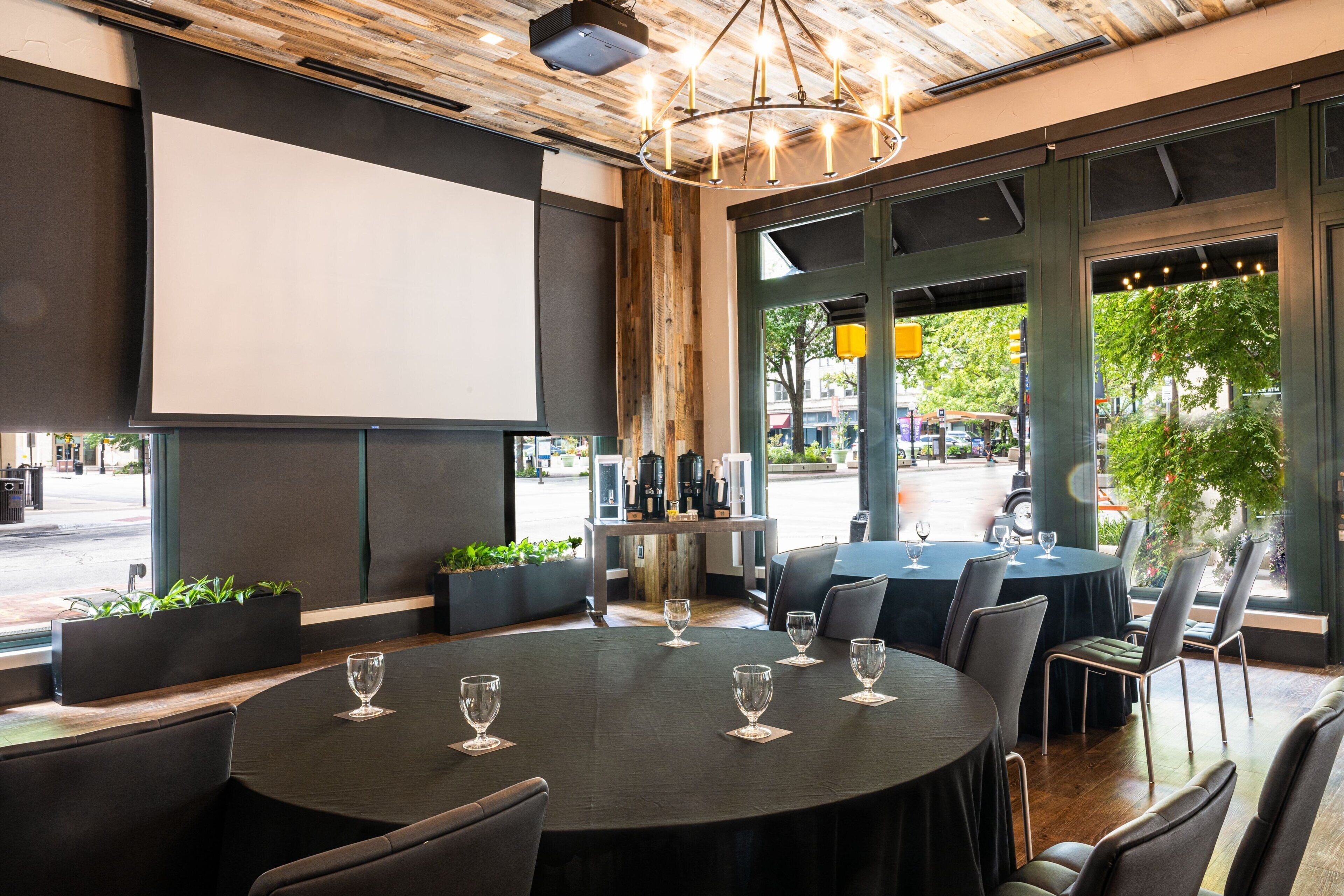A restaurant with round tables, chairs, and a projector screen.