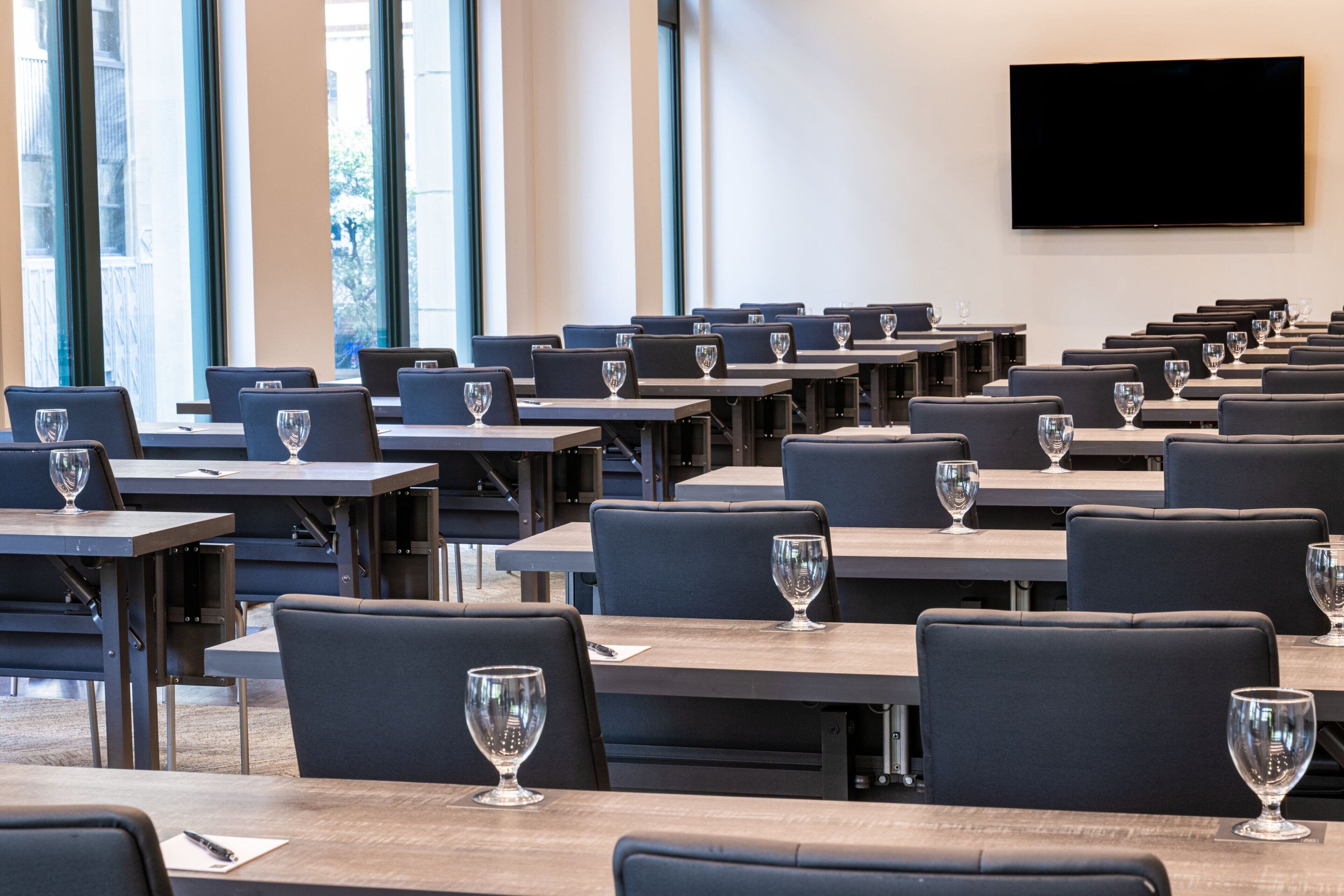 Une salle de conférence avec des rangées de tables et de chaises, chacune étant équipée d’un verre à vin.