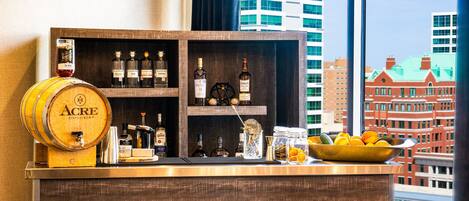 A bar area with a wooden barrel, shelves of liquor bottles, and a bowl of citrus fruits.