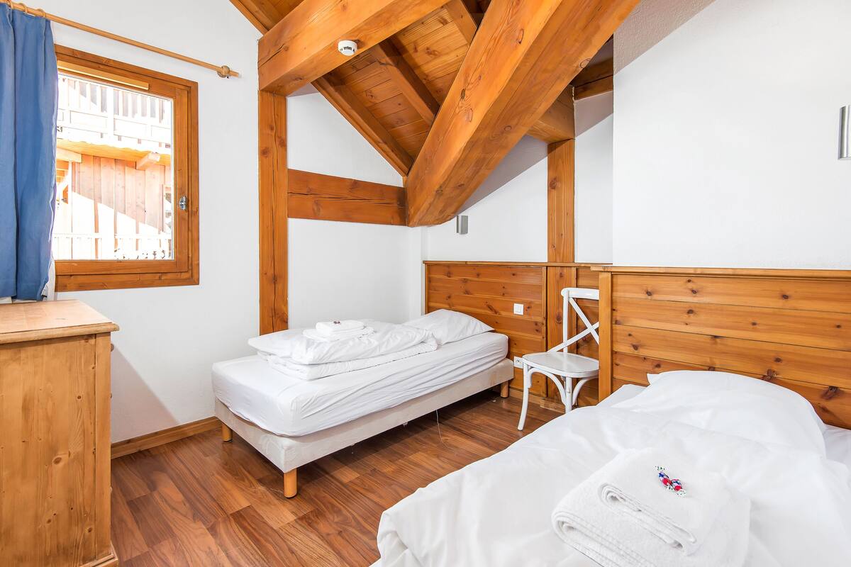 Un dormitorio con techo de madera, una cama individual, una mesita de noche de madera y una ventana con cortina.