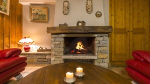 Una habitación acogedora con chimenea de piedra, una mesa de madera con velas y sofás de cuero rojo.