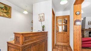 Zona de recepción con mostrador de madera, un cuadro enmarco, planta en maceta y puerta de madera que da a otra habitación.