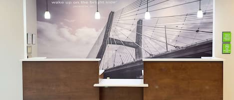 A reception desk with a large mural of a bridge, pendant lighting, and a sign indicating check-in hours.