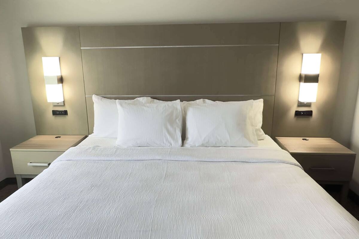 A hotel room with a large bed, two bedside tables, and wall-mounted lamps.