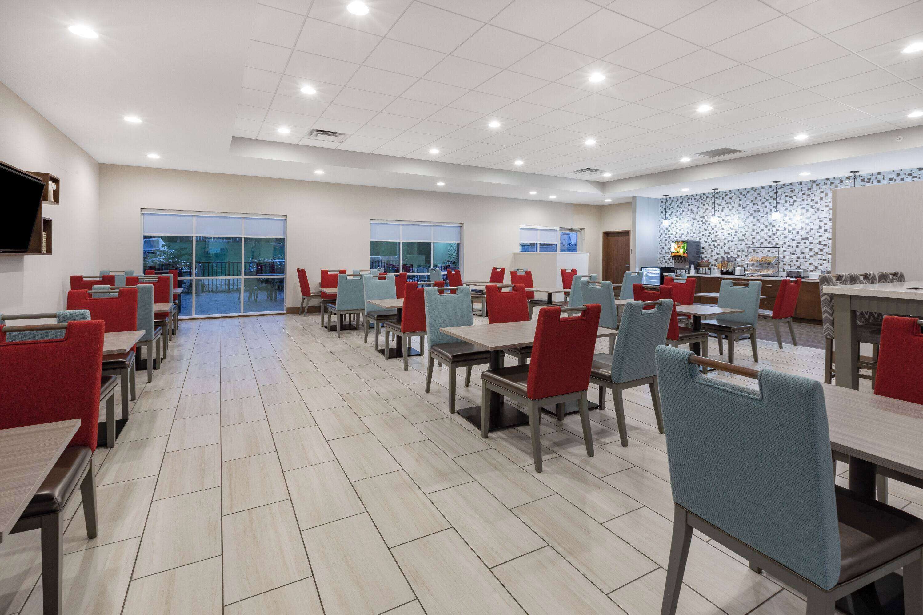 A spacious dining area with multiple tables and chairs, large windows, and a tiled floor.