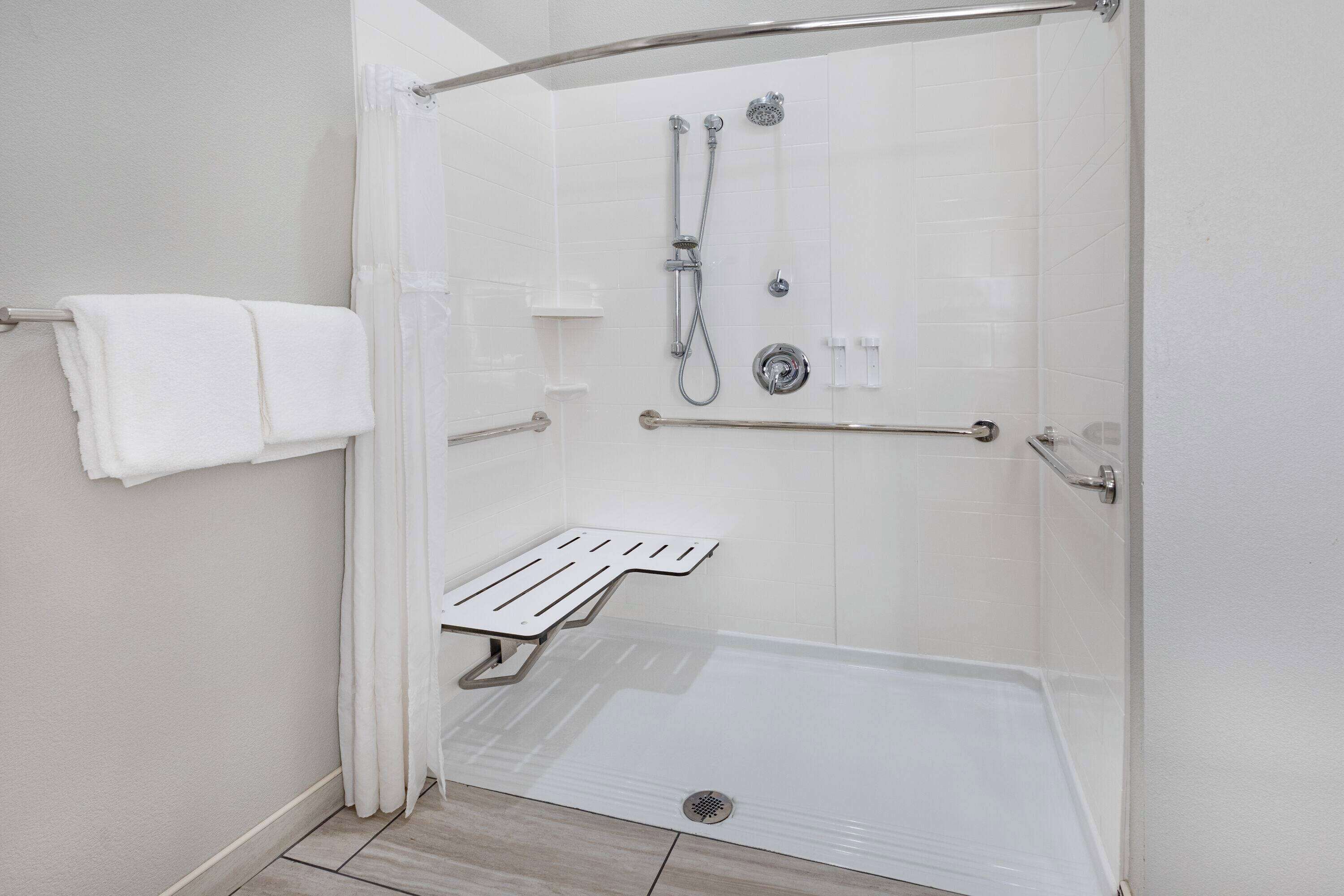 A wheelchair-accessible shower stall with a grab bar, a bench, and a hand-held showerhead.