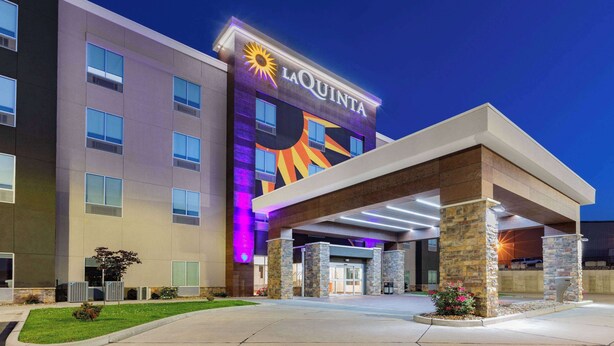 Entrada de un hotel con un cartel grande que dice "LAQUINTA" y un gráfico de sol.