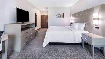 A hotel room with a bed, bedside table, TV, wardrobe, and artwork on the wall.