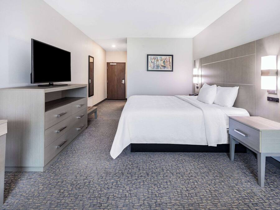 A hotel room with a bed, bedside table, TV, wardrobe, and artwork on the wall.