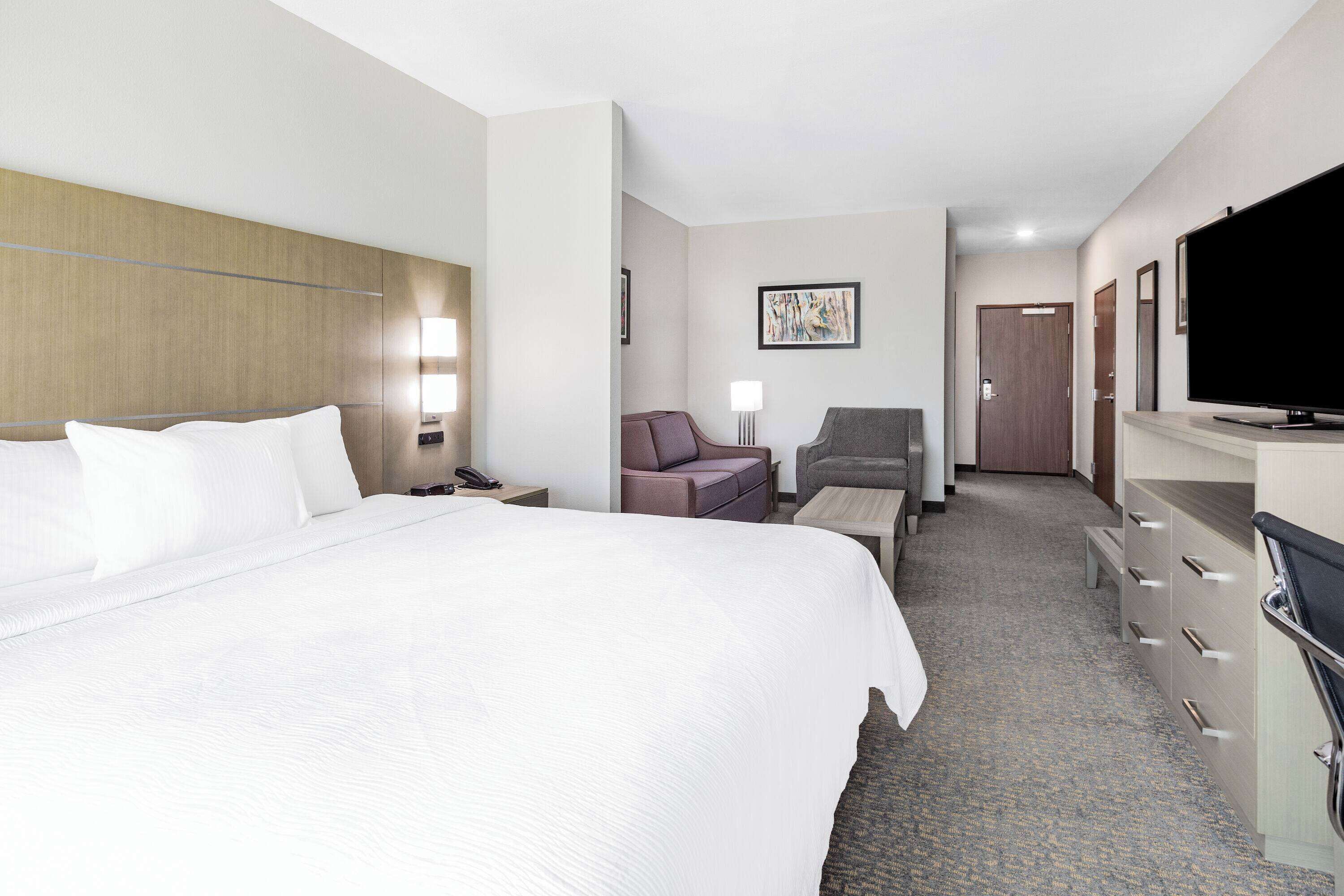 A hotel room with a large bed, a desk, a chair, a television, and a wardrobe.
