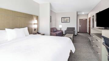 A hotel room with a large bed, a desk, a chair, a television, and a wardrobe.