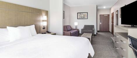 A hotel room with a large bed, a desk, a chair, a television, and a wardrobe.