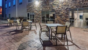 Un patio al aire libre con mesas y sillas, un muro de piedra y ventanas grandes.