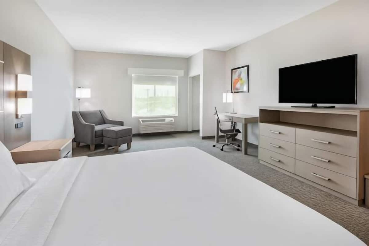 Ein Hotelzimmer mit einem großen Bett, einem Schreibtisch, einem Sessel, einem Fernseher und einem Fenster.