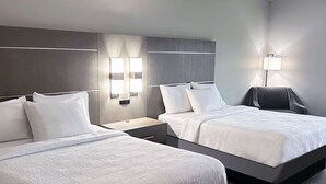 Habitación de hotel con dos camas, una mesita de noche, una lámpara y una silla.